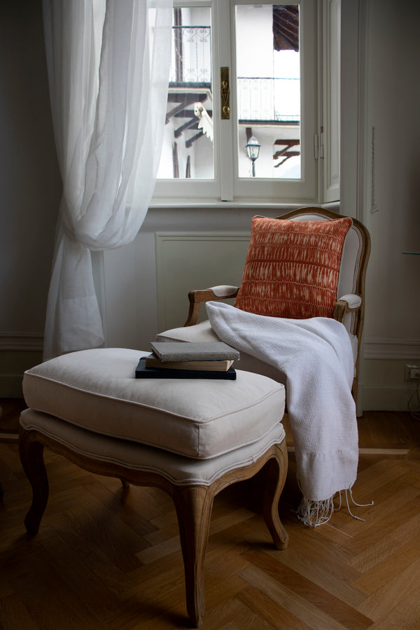 Orange Cushion atop a cream armchair with luxurious blanket